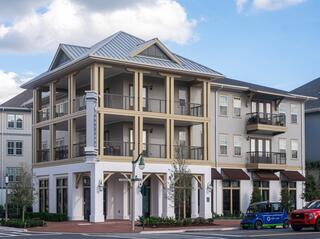 A modern multi-story building features balconies, large windows, and a welcoming facade, set in a landscaped area with parked cars.