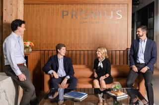 A casual business meeting takes place in a stylish office, featuring four professionals engaged in conversation on a leather sofa.