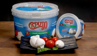 Containers of fresh Caputo mozzarella, including nodini and mini sizes, displayed alongside ripe cherry tomatoes and basil on a black platter.