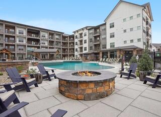 A modern courtyard features a sparkling pool, cozy fire pit, and stylish seating, surrounded by contemporary apartment buildings.