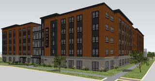 A modern, multi-story building features a mix of dark wood and stone exteriors, large windows, and landscaped green areas.