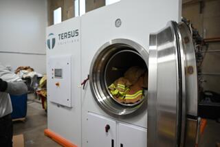 A large industrial machine designed for cleaning, featuring a round door and safety equipment inside, labeled "Tersus Solutions."