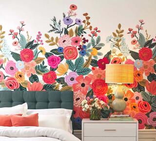 A vibrant floral mural decorates a bedroom wall, complementing a green headboard and a bedside table with a lamp and flower vase.