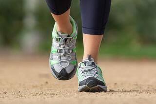 A close-up of a foot in a sporty shoe, walking on a dirt path, showcasing the shoe's vibrant green and gray design.