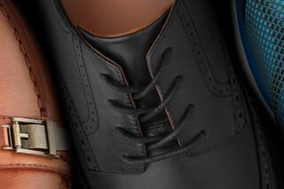 A close-up view of three shoes: a sleek black dress shoe with laces, a brown shoe with a buckle, and a blue mesh shoe.