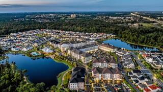 Aerial view of a suburban community with neat homes, winding roads, and serene lakes, surrounded by lush greenery and distant cityscape.